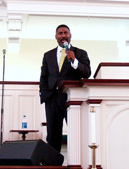 Man in black suit preaching and speaking jpg